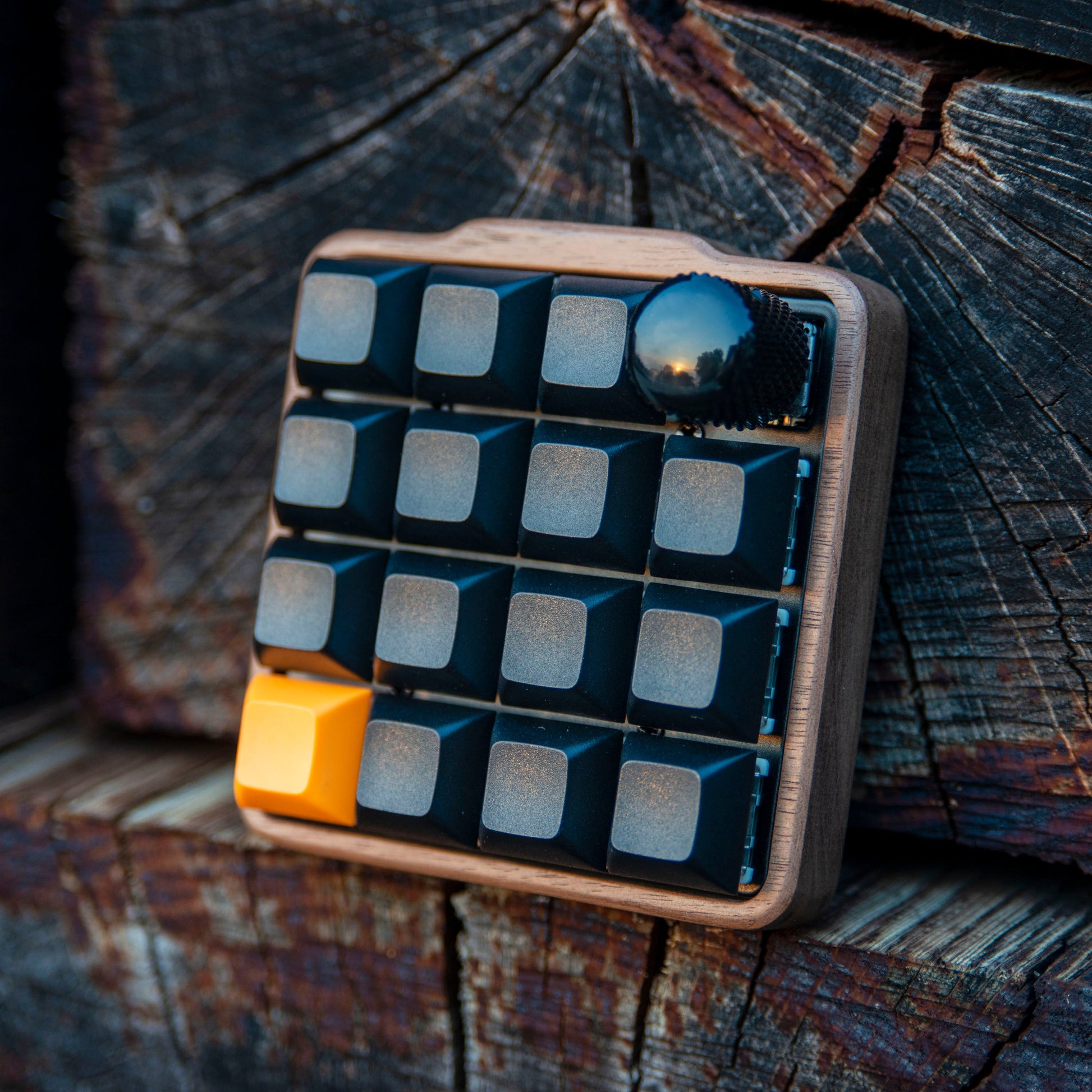 Small keyboard with black keys and an orange escape key on a wooden surface